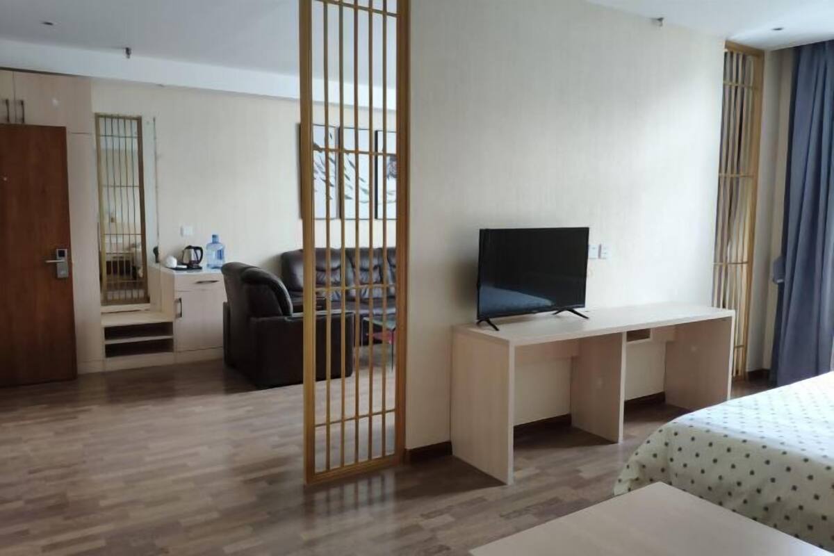 Une chambre d’hôtel avec un plancher en bois, un bureau avec une télévision, un lit recouvert d’une courtepointe à motifs, une cloison en bois et une vue sur l’extérieur.