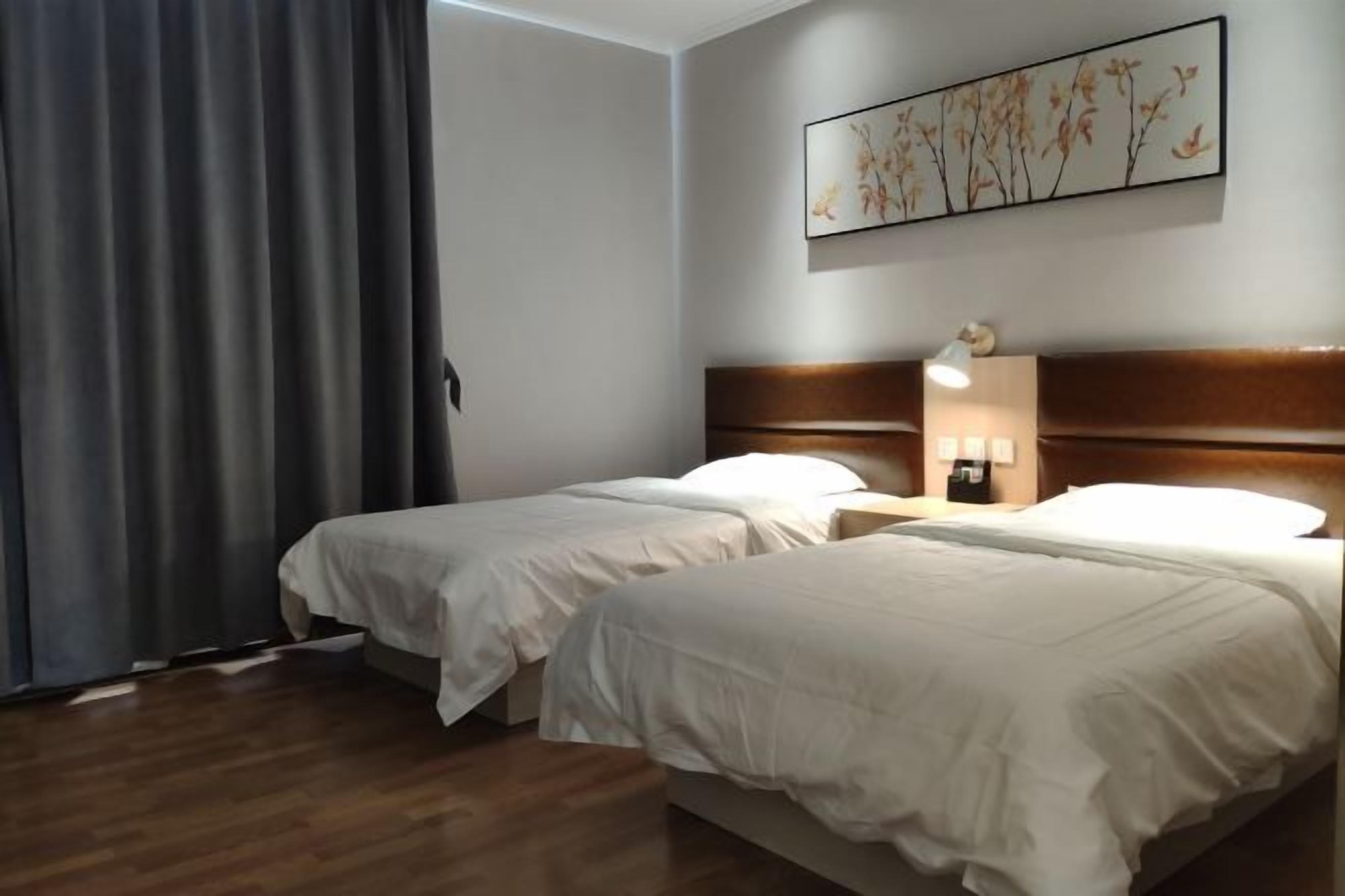 Quarto de hotel com duas camas, cabeceira de madeira, mesa de cabeceira com abajur e obra de arte na parede.