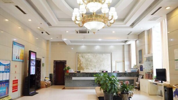 Een ruime lobby met een receptiebalie, een kroonluchter en potplanten.
