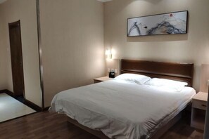 A hotel room with a large bed, a nightstand, a wall-mounted lamp, and a painting above the bed. - Chenguang Hotel (Shijiazhuang)