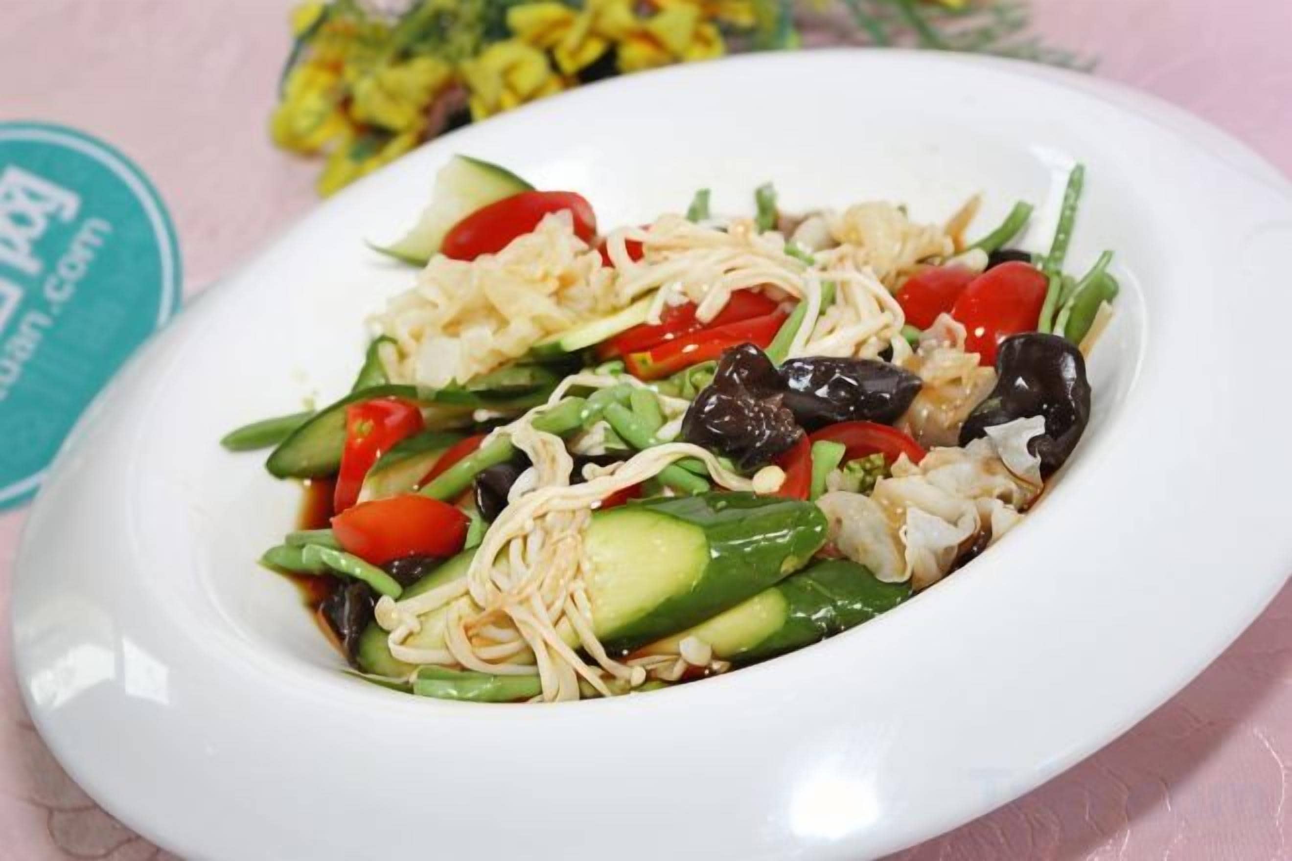 A white plate with a noodle dish containing vegetables and black olives.