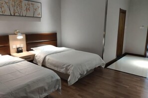 A hotel room with two beds, a wooden headboard, a bedside table with a lamp, and a wall-mounted artwork. - Chenguang Hotel (Shijiazhuang)