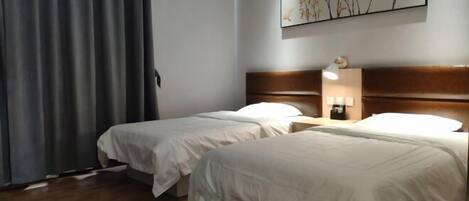 A hotel room with two beds, a wooden headboard, a nightstand with a lamp, and a wall-mounted artwork.