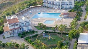 Vista aérea de un complejo turístico con piscina, varias edificaciones y palmeras.