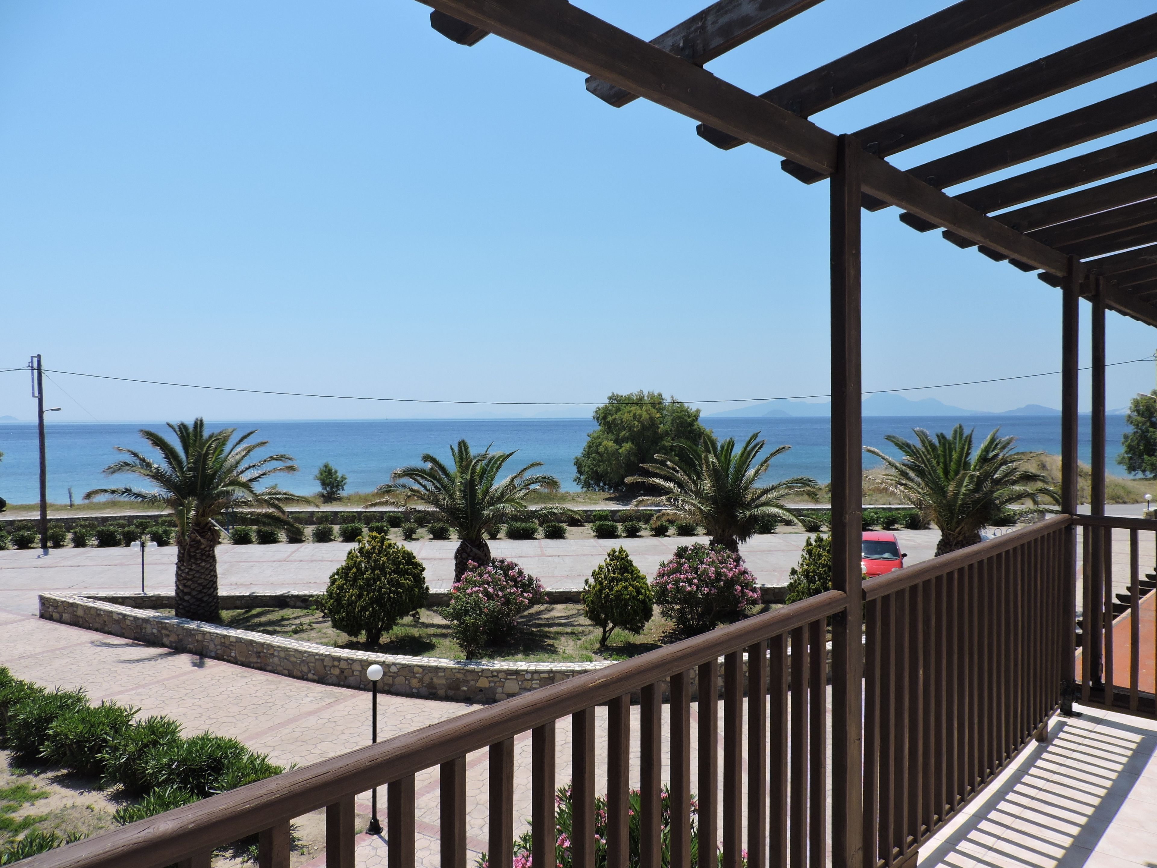 Ein Balkon mit Blick auf das Meer, Palmen und einen Parkplatz.