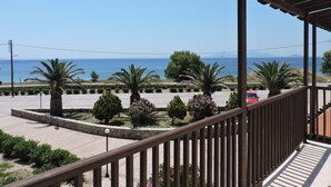 Un balcón con vistas al mar, palmeras y un estacionamiento.