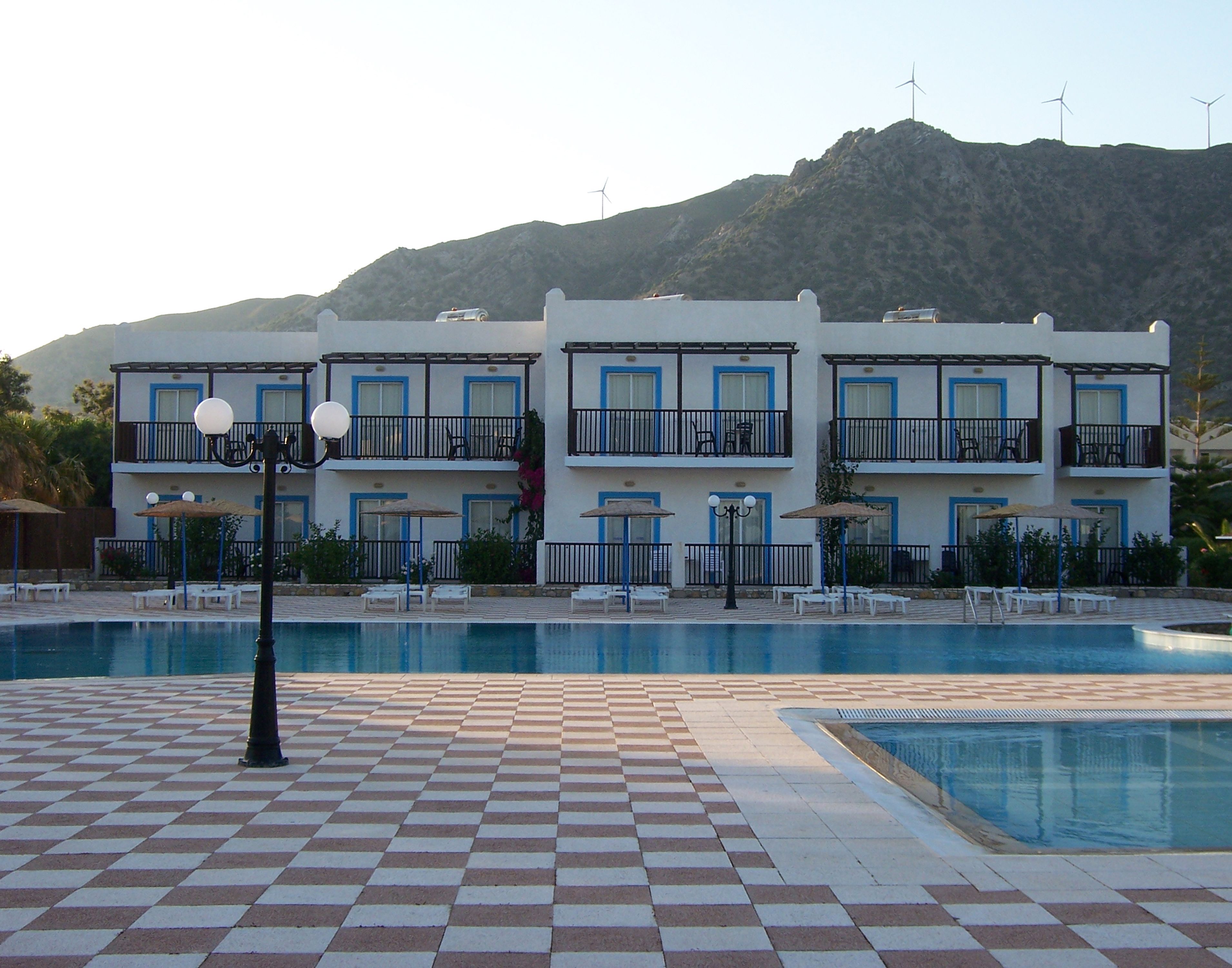 Ein Hotel mit Poolbereich, mehreren Balkonen und Windkraftanlagen im Hintergrund.