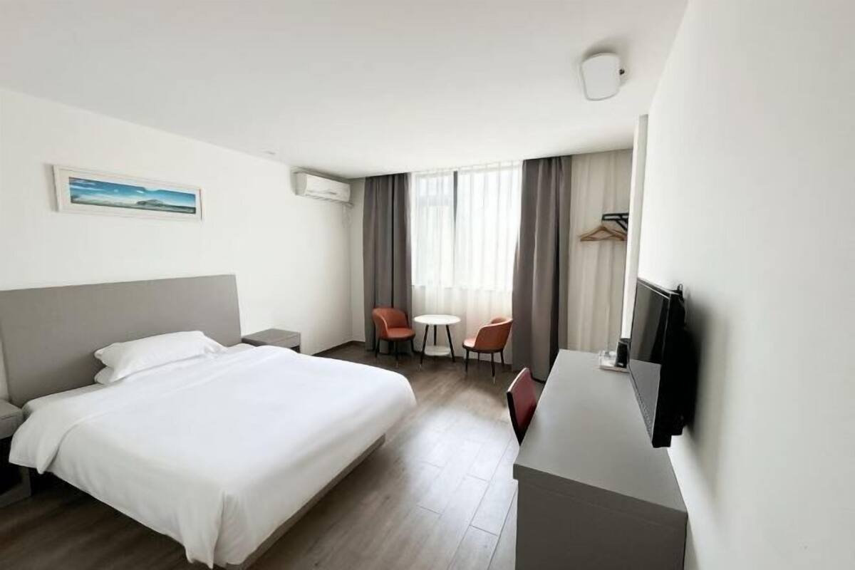 A hotel room with a bed, a desk, a chair, a TV, and a window with curtains.