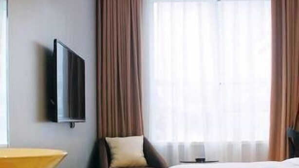 A hotel room with a bed, a TV mounted on the wall, a chair, and a window with curtains. - Hi Inn (Chengdu)