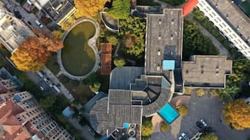 An aerial view of a building with a curved roof, a central courtyard, and surrounding trees.