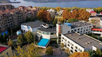 A multi-story hotel with a parking lot, surrounded by trees and buildings, overlooking a body of water.