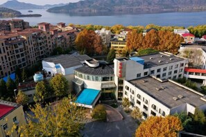 A multi-story hotel with a parking lot, surrounded by trees and buildings, overlooking a body of water. - Shuangyang Hotel (Huairou)