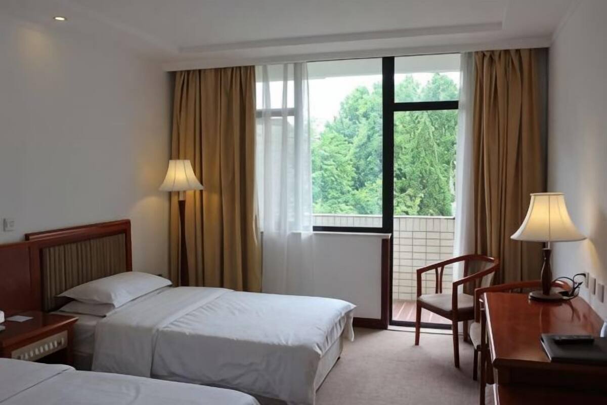 A hotel room with two beds, a desk, a chair, and a window with curtains.