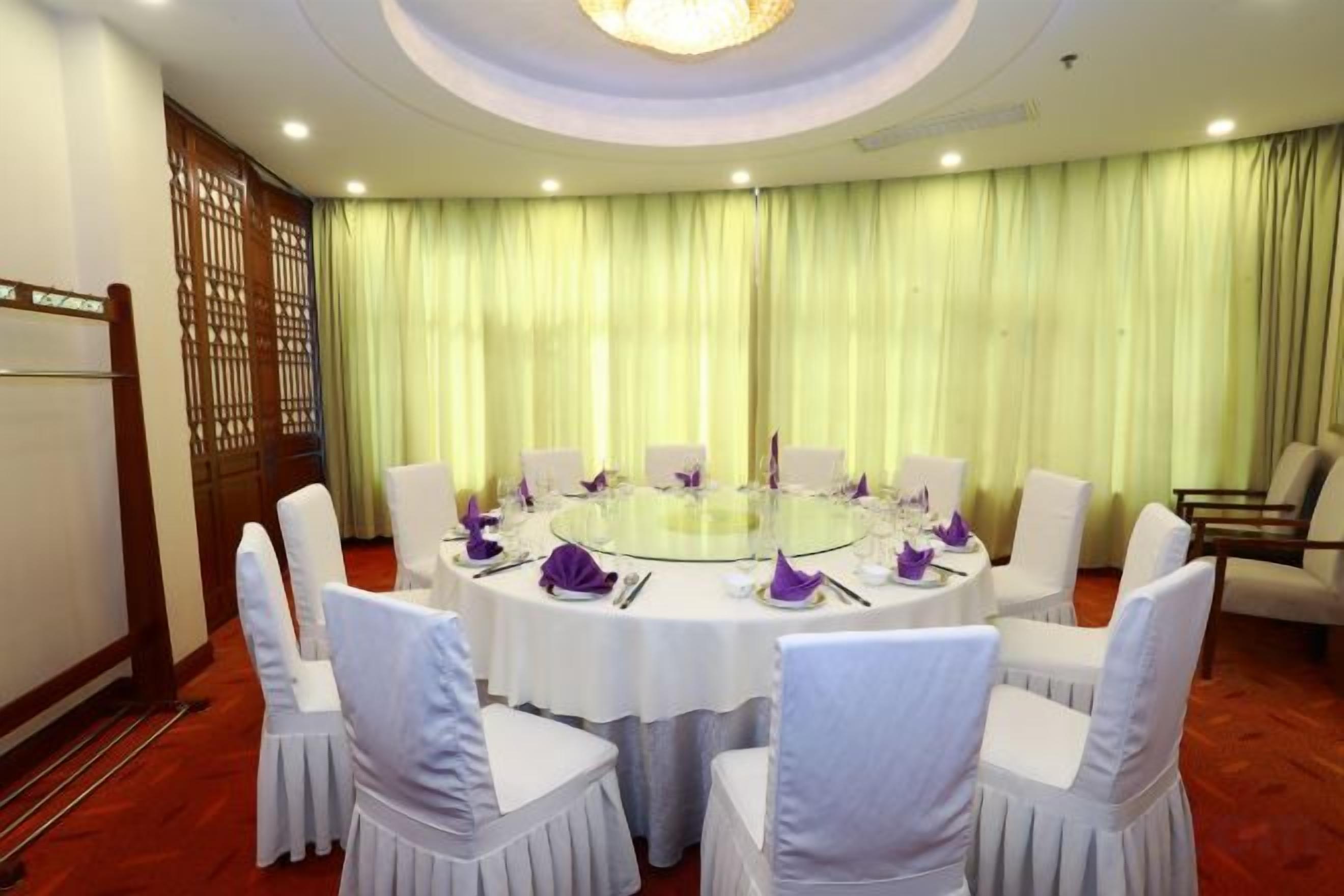 A conference room with a round table, white chairs, and a green curtain backdrop.