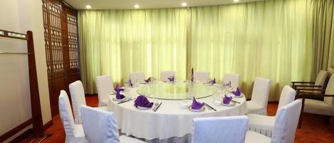 A conference room with a round table, white chairs, and a green curtain backdrop.