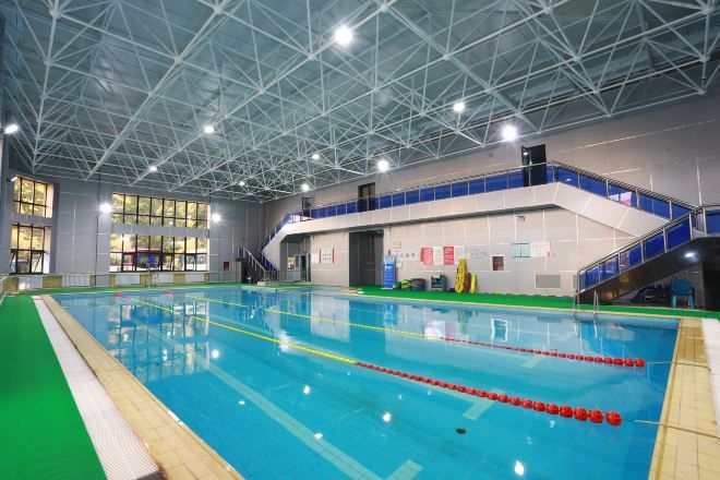An indoor swimming pool with a high ceiling and a staircase leading to an upper level.