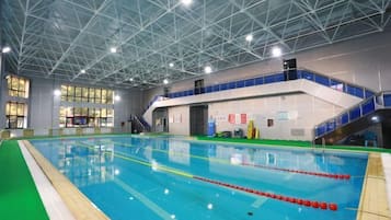 An indoor swimming pool with a high ceiling and a staircase leading to an upper level.