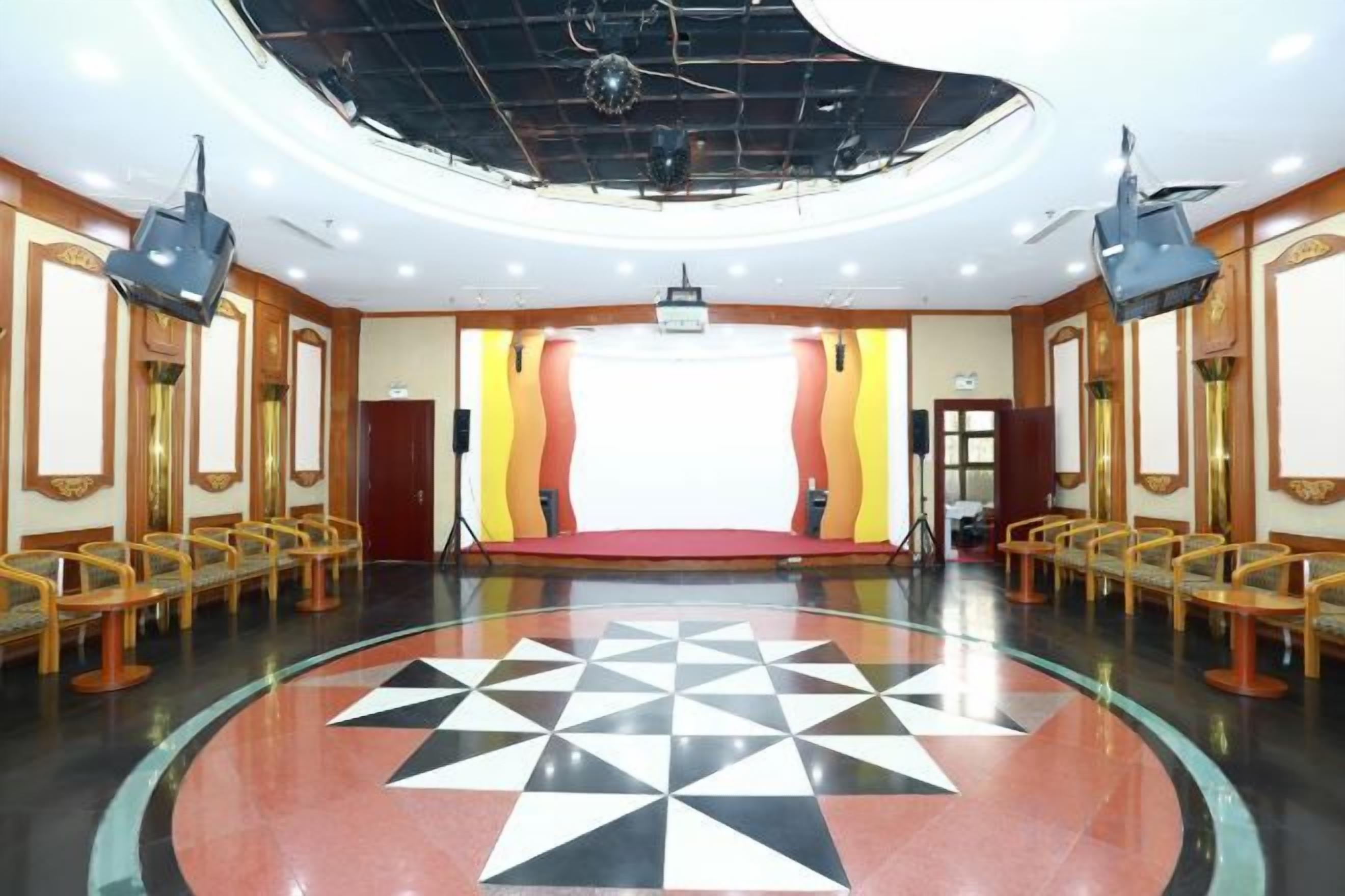 Un salón de conferencias con un escenario, filas de sillas y un piso con diseño de cuadros.