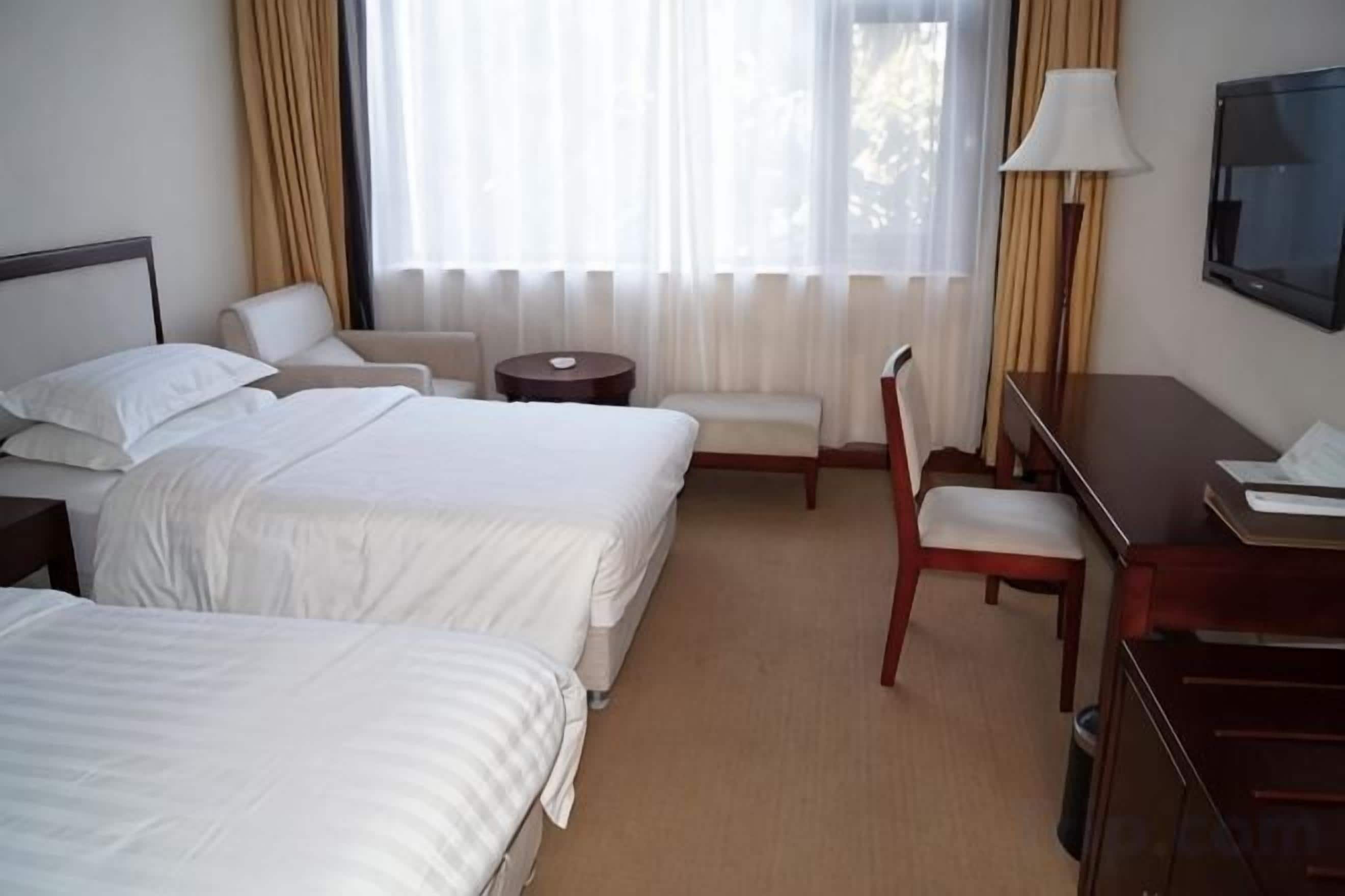 Hotellihuone, jossa on kaksi sänkyä, työpöytä, tuoli, pieni pyöreä pöytä ja televisio.