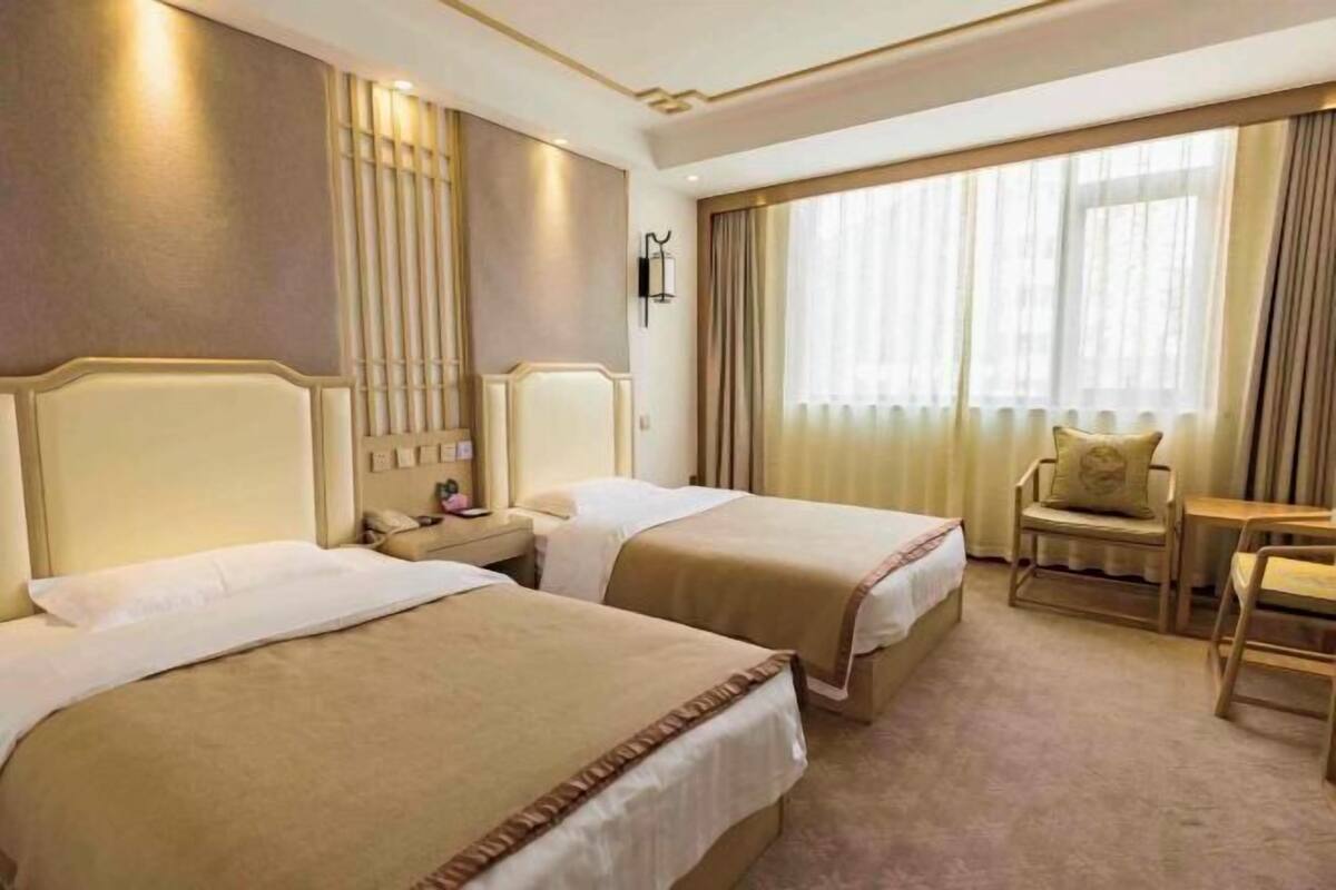 A hotel room with two beds, a desk, a chair, and a large window with curtains.