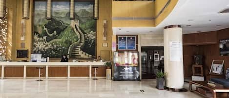 A hotel lobby with a reception desk, a large mural, a staircase, and a seating area.