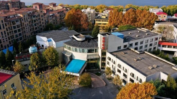 A high-rise hotel with multiple floors, a swimming pool, and a view of a lake and mountains. - Shuangyang Hotel (Huairou)