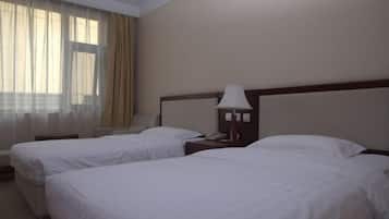Een hotelkamer met twee bedden, een nachtkastje met een lamp, een telefoon en een raam met gordijnen.