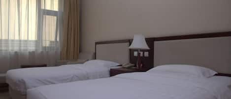 A hotel room with two beds, a nightstand with a lamp, a telephone, and a window with curtains.