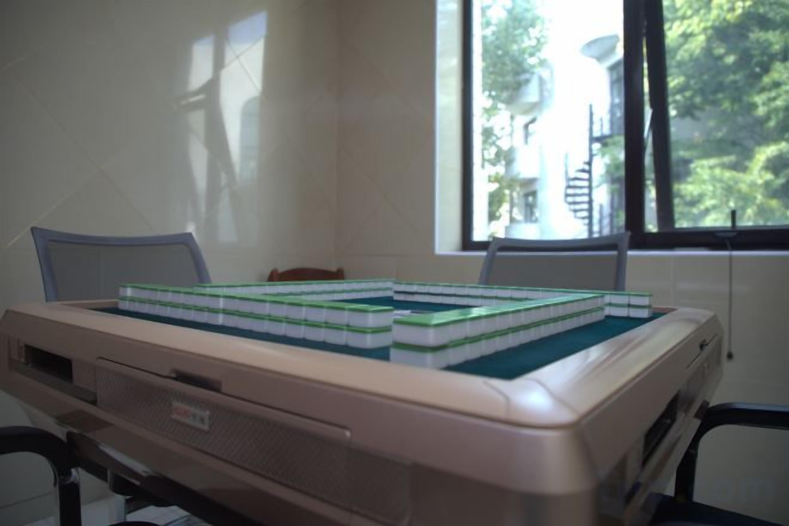 A computer with a chessboard on top, a window with a view of trees, and a chair.