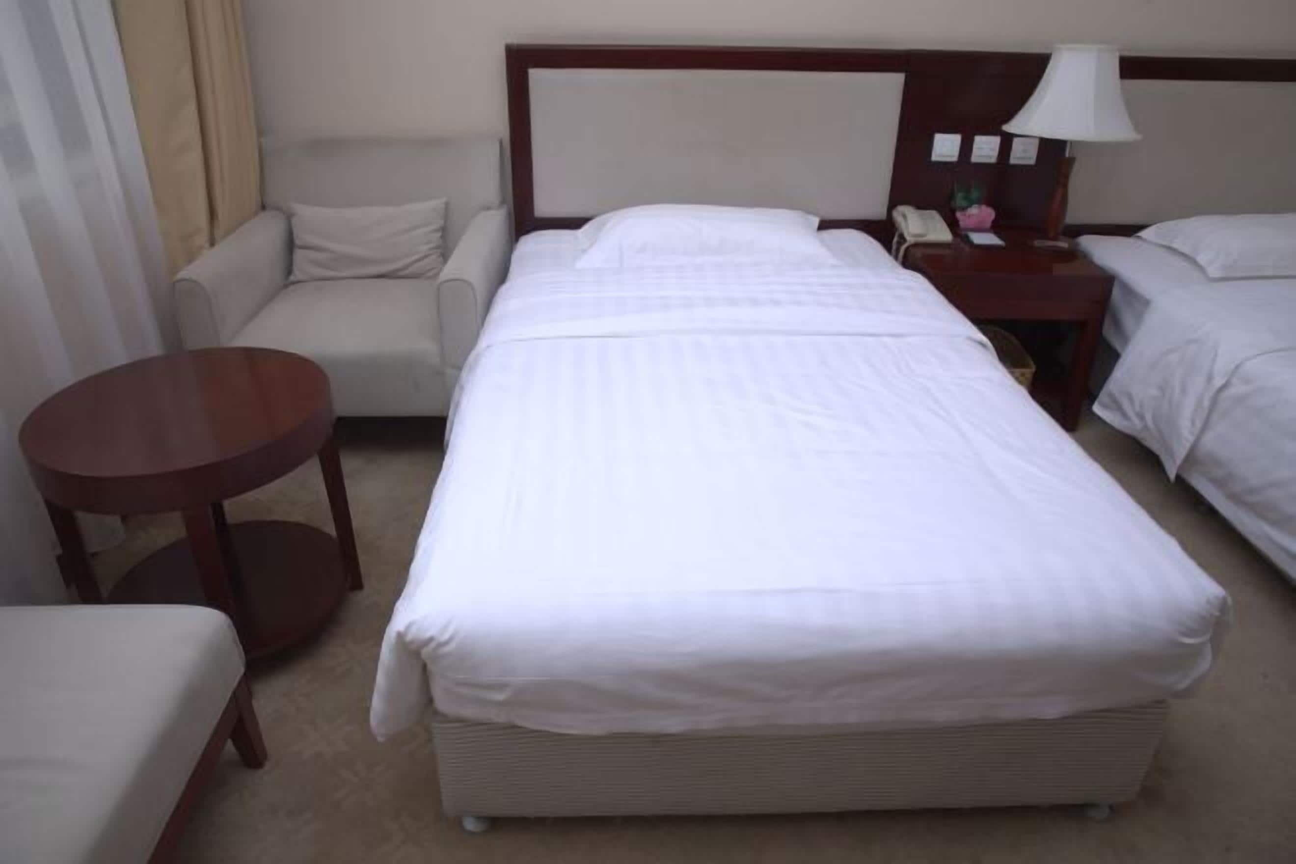 A hotel room with a large bed, a small round table, a sofa, and a nightstand with a lamp.