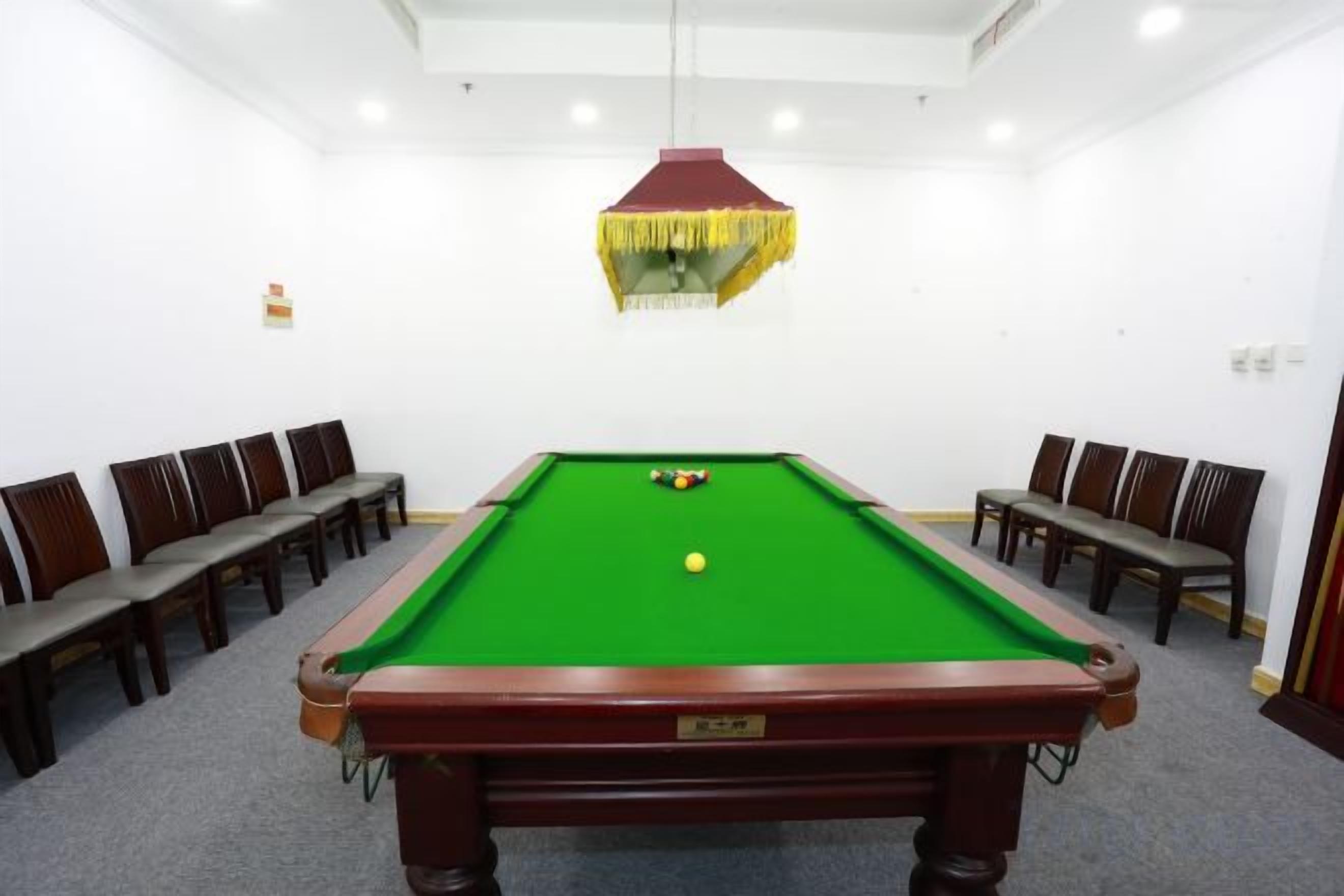A pool table with chairs around it in a room with white walls and a hanging light fixture.