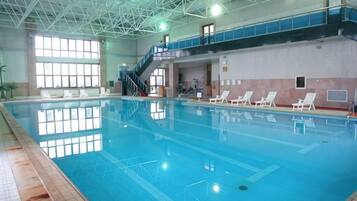 En inomhuspool med klart vatten, ett kaklat golv och en trappa som leder upp till en balkong.