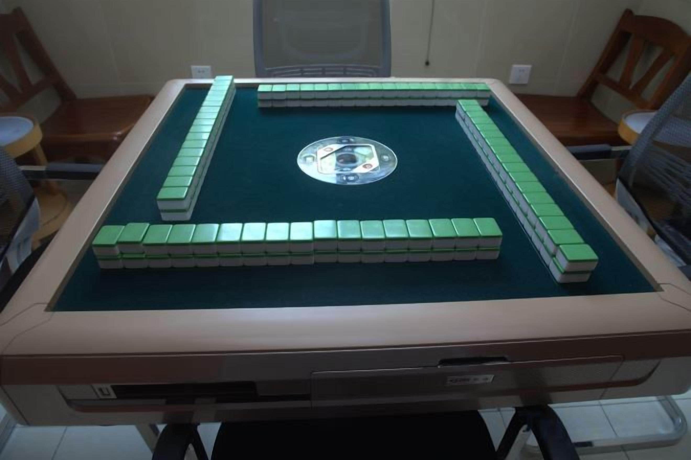 Una mesa de billar con fieltro verde, rodeada de sillas, en una habitación con piso de baldosas.