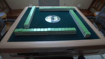 Una mesa de billar con fieltro verde, rodeada de sillas, en una habitación con piso de baldosas.