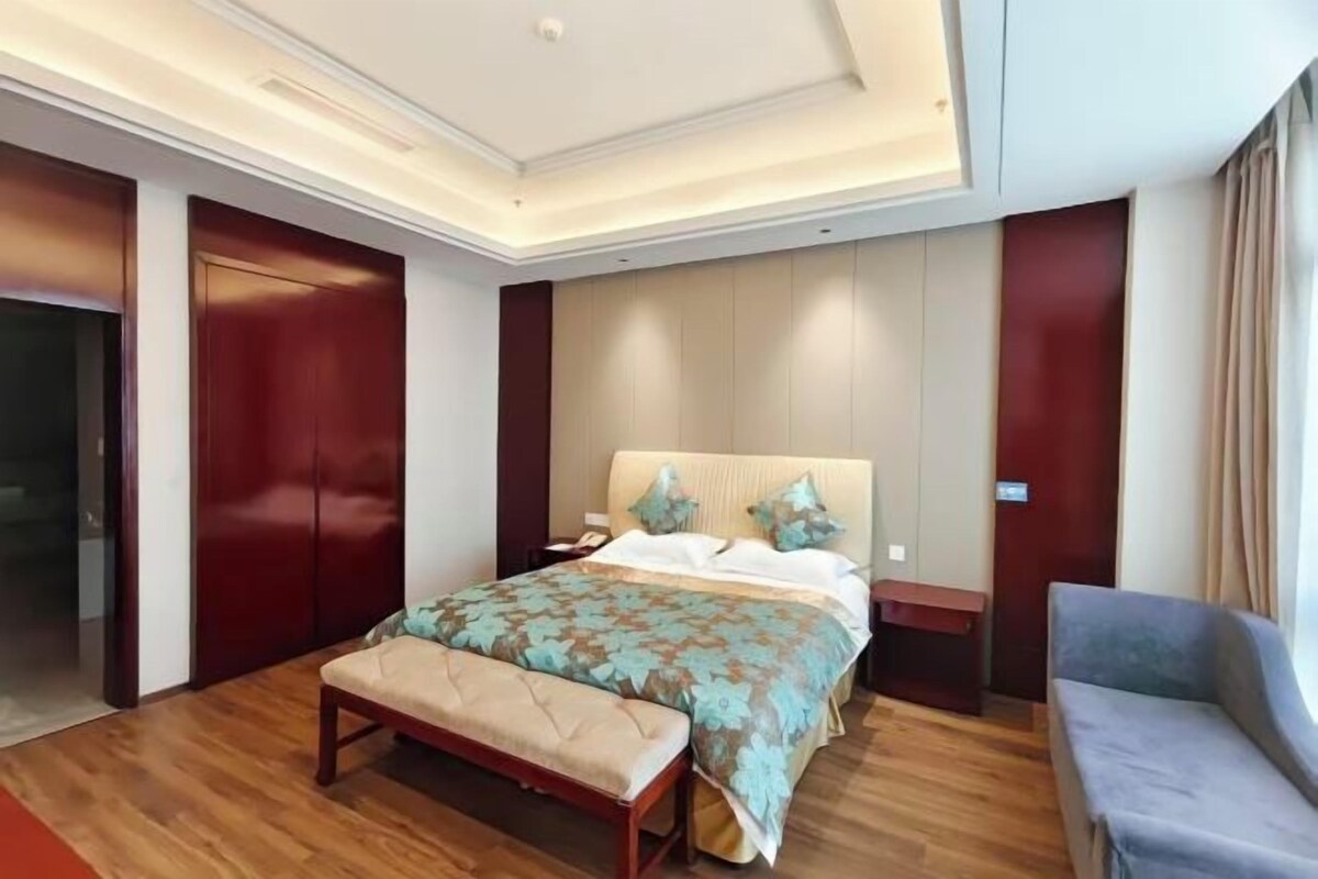 A hotel room with a large bed, a bench, a sofa, and a desk.