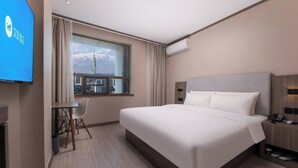A hotel room with a bed, a desk with a chair, a TV, a window with curtains, and an air conditioning unit. - Hanting Hotel (Nanjing)