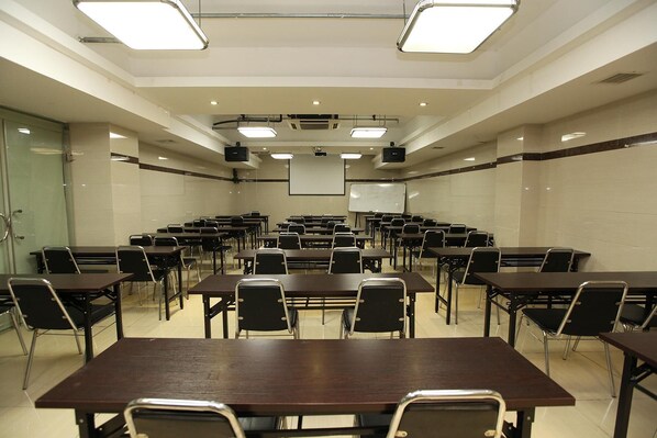 A conference room with multiple tables and chairs, a whiteboard, and a projector screen.