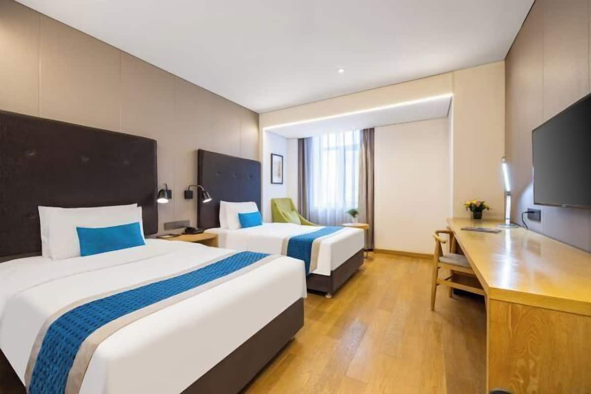 A hotel room with two beds, a desk, a chair, a TV, and a window with curtains.