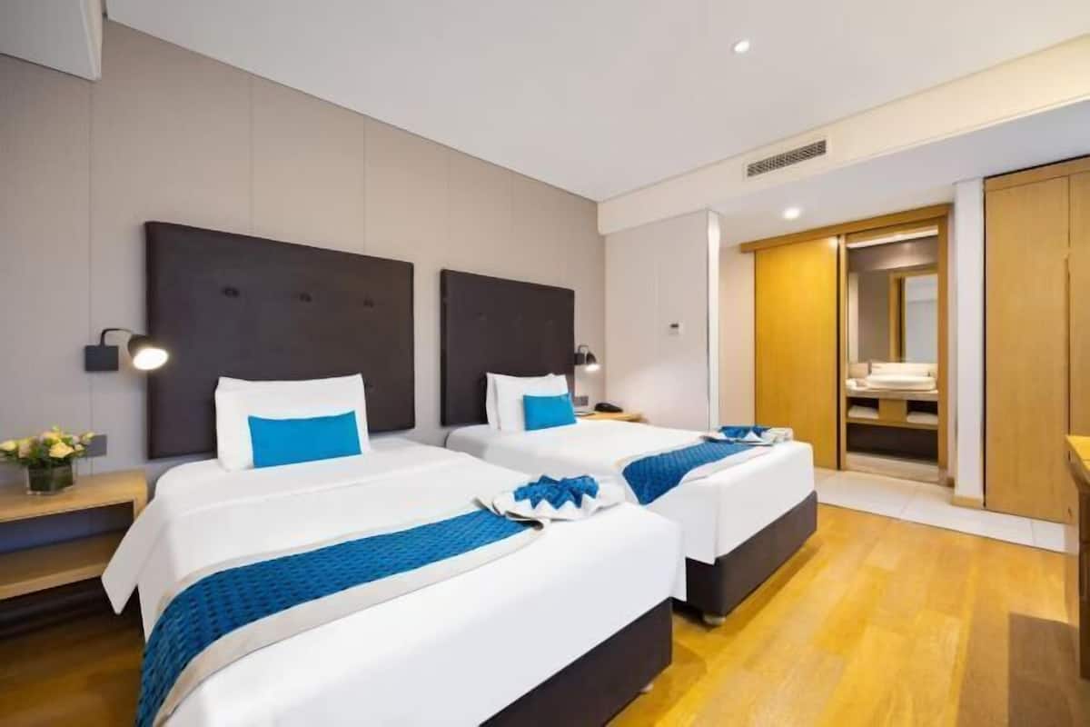 A hotel room with two beds, a wooden floor, a wardrobe, and a mirror.