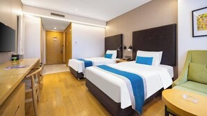 A hotel room with two beds, a desk, a chair, and a TV.