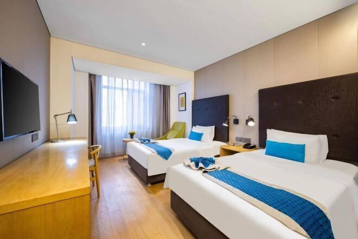 A hotel room with two beds, a desk, and a TV.