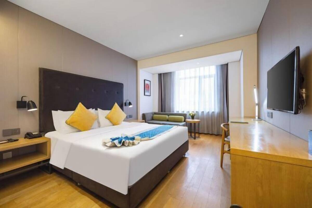 A hotel room with a large bed, a desk, a TV, and a sofa.