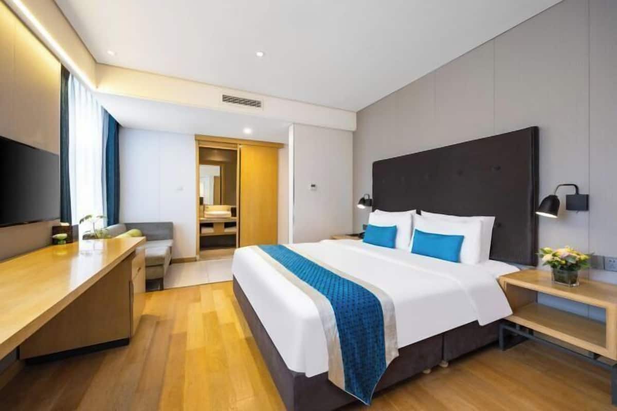 A modern hotel room with a large bed, bedside tables, a desk, and a TV.