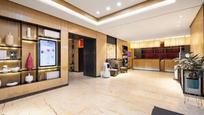 A modern hotel lobby with marble flooring, wooden shelving with decorative items, a seating area, and a reception desk.