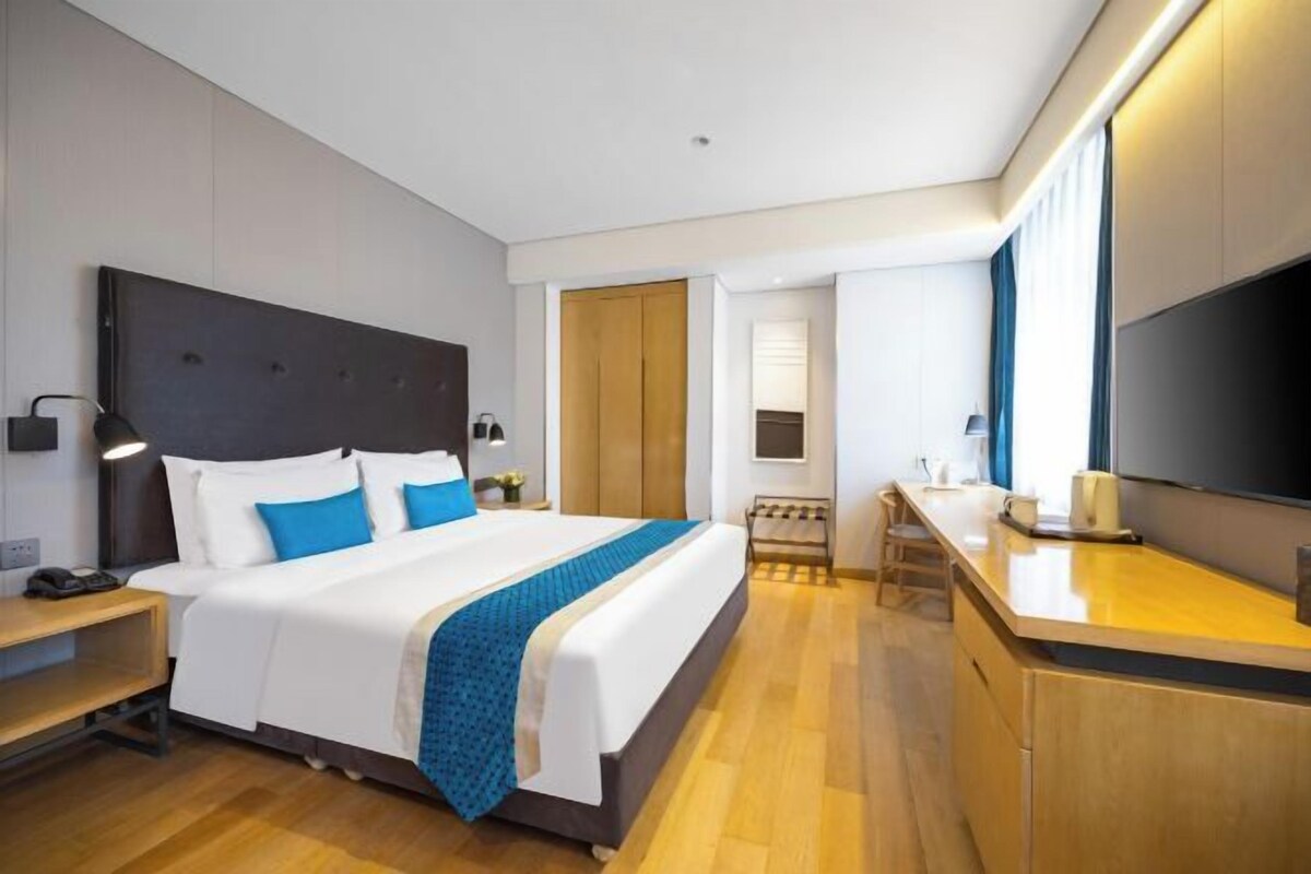 A modern hotel room with a large bed, bedside tables, a desk, and a flat-screen TV.