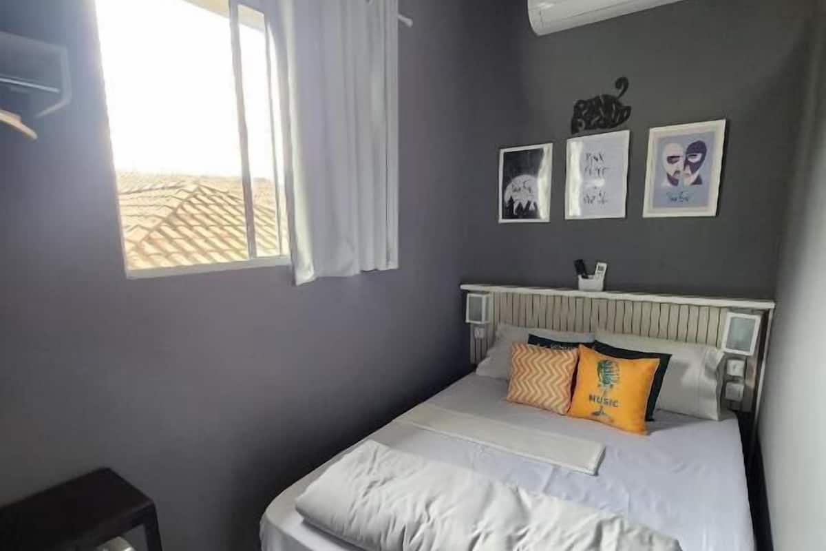Ein Schlafzimmer mit Bett, Schreibtisch, einem Fenster mit Vorhängen und Wandbildern.