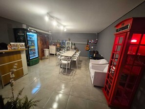 A room with a dining table, chairs, a refrigerator, a telephone booth, and a guitar.