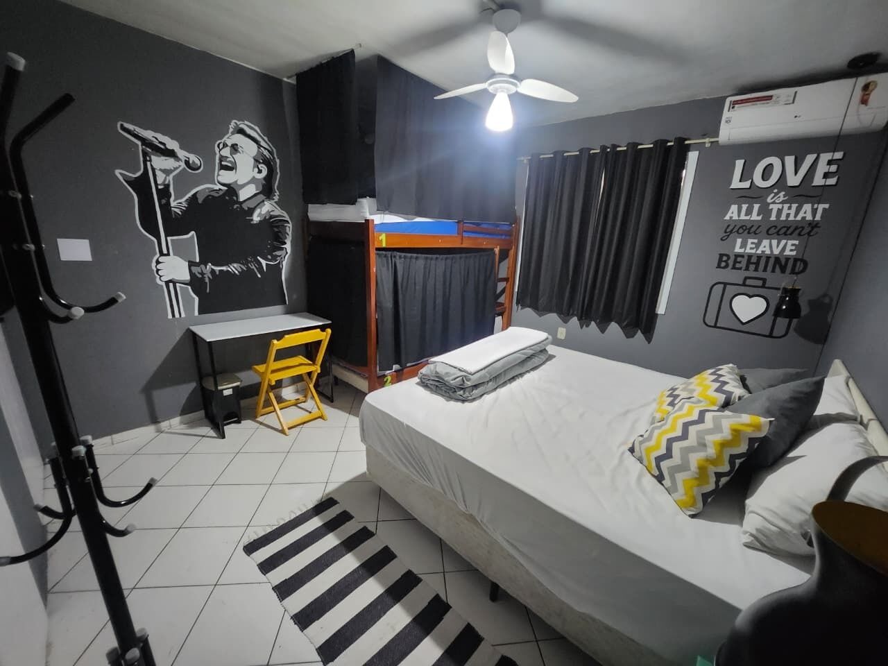 A bedroom with a bunk bed, a desk, a chair, a bed with pillows, a striped rug, a ceiling fan, and a wall with a motivational quote.
