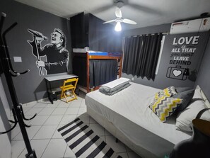 A bedroom with a bunk bed, a desk, a chair, a bed with pillows, a striped rug, a ceiling fan, and a wall with a motivational quote.