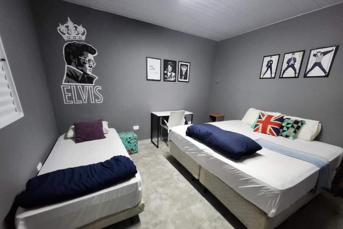 Ein Zimmer mit zwei Betten, einem Schreibtisch und einem Stuhl. An den Wänden hängen Bilder in Rahmen und ein Wandtattoo von Elvis Presley.